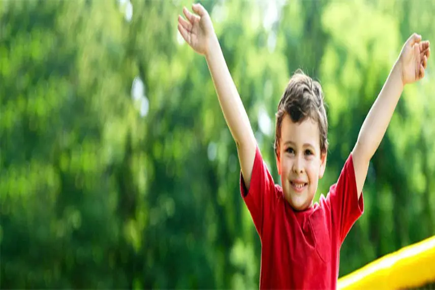 A smiling child with arms raised, symbolizing joy and accomplishment, outdoors.