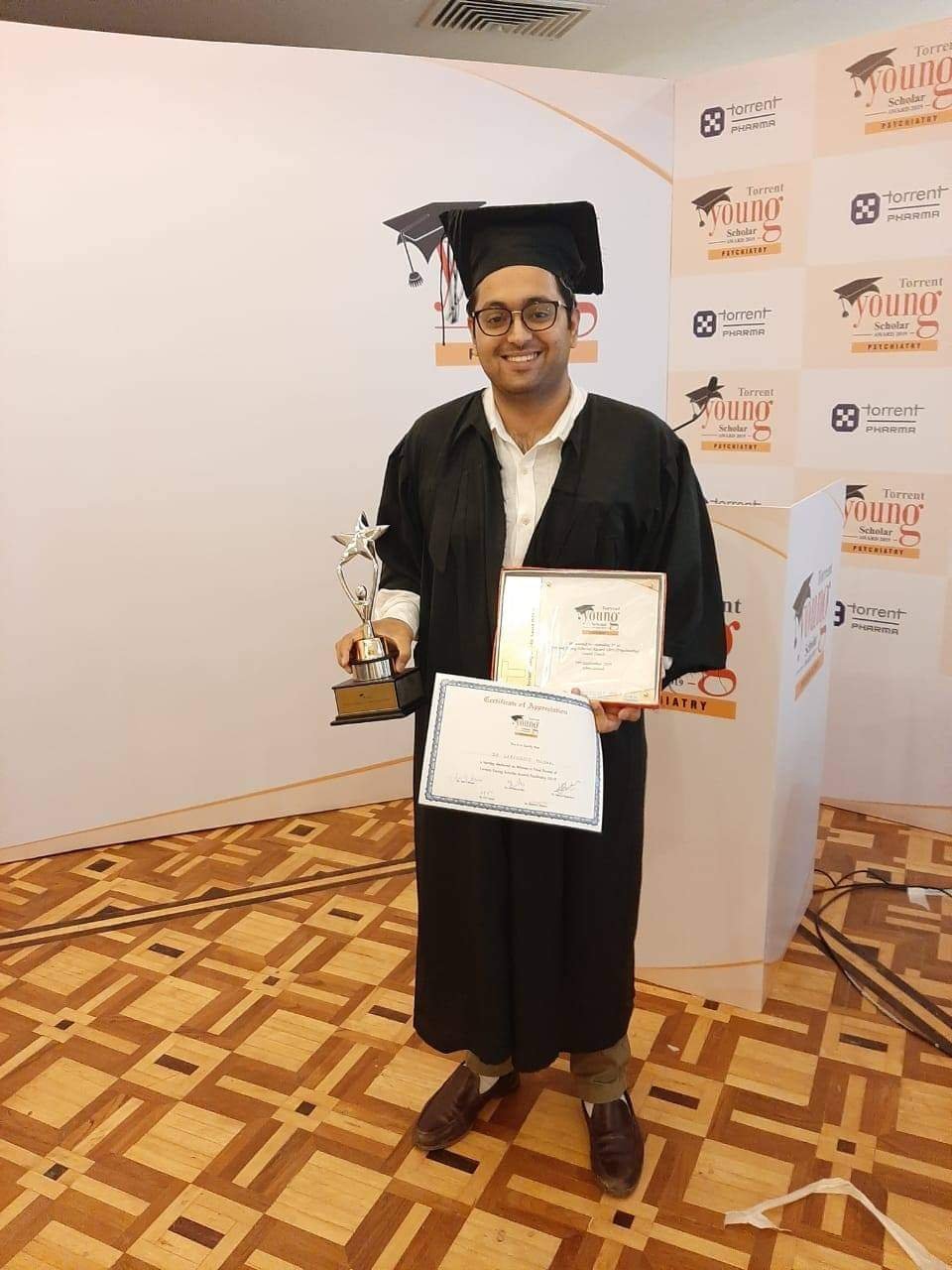 Dr. Varchasvi Mudgal holding a certificate and award at a recognition event.