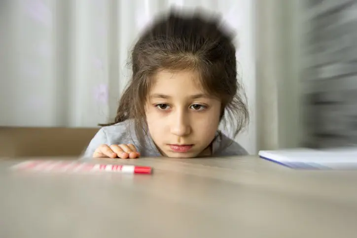 A young girl looking focused and anxious, possibly showing signs of obsessive-compulsive behavior, staring at an object.