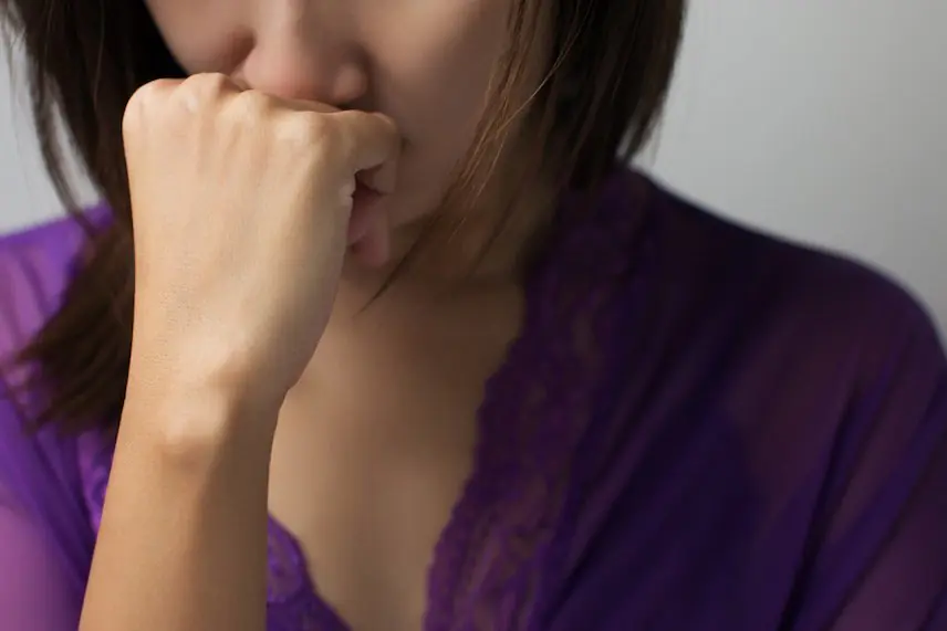 A woman sitting and holding her fist near her face, appearing deep in thought or distress, possibly reflecting the emotional toll of depression.