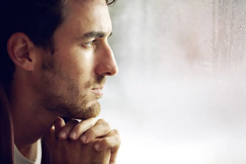 A man sitting pensively by a window, possibly experiencing anxiety or deep contemplation.