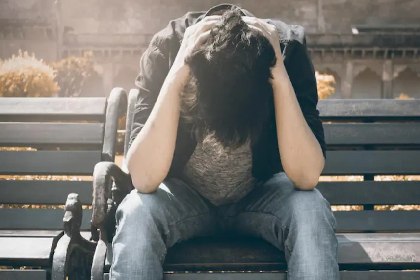 A young man sitting on a bench, holding his head in distress, indicating emotional turmoil.