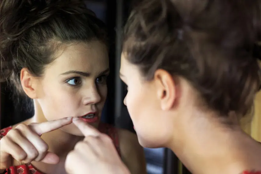 A woman looking at her reflection in the mirror, possibly exhibiting signs of intense emotions related to bipolar disorder.