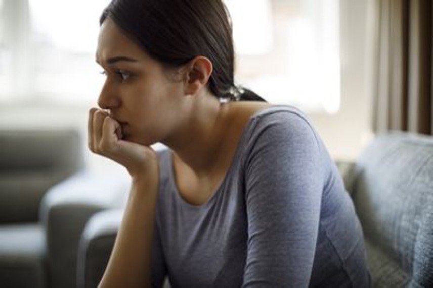 A woman sitting on a couch, looking thoughtful or distressed, deep in thought.