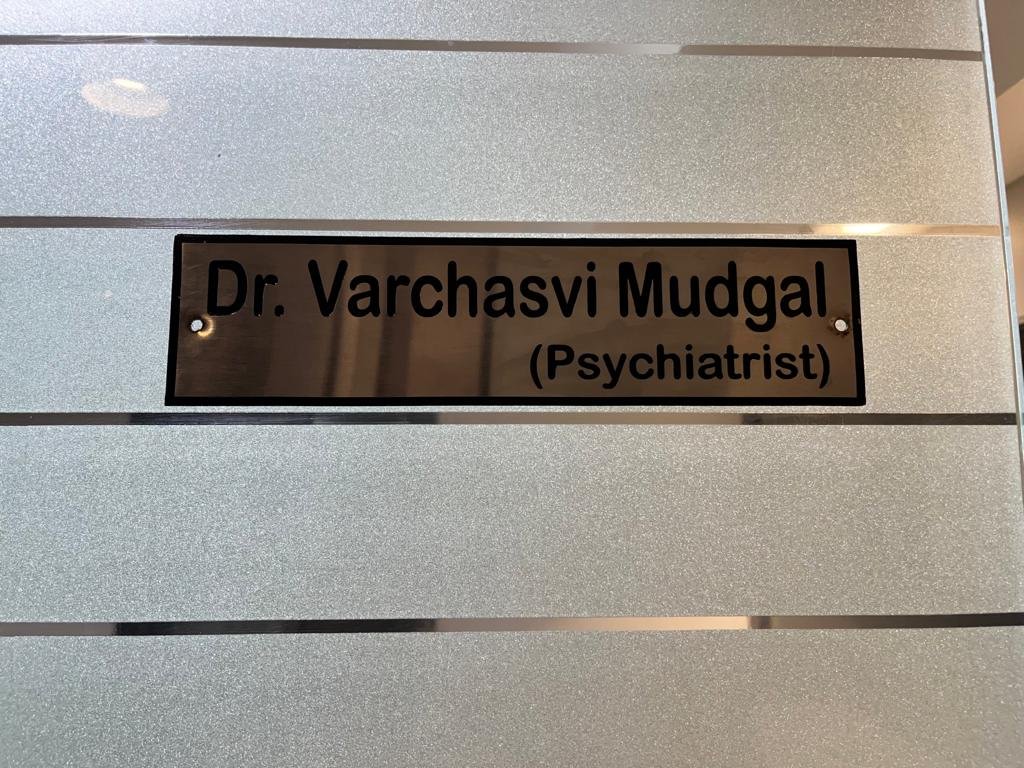 "Nameplate displaying Dr. Varchasvi Mudgal's name and designation as a psychiatrist in a clean office setting."
